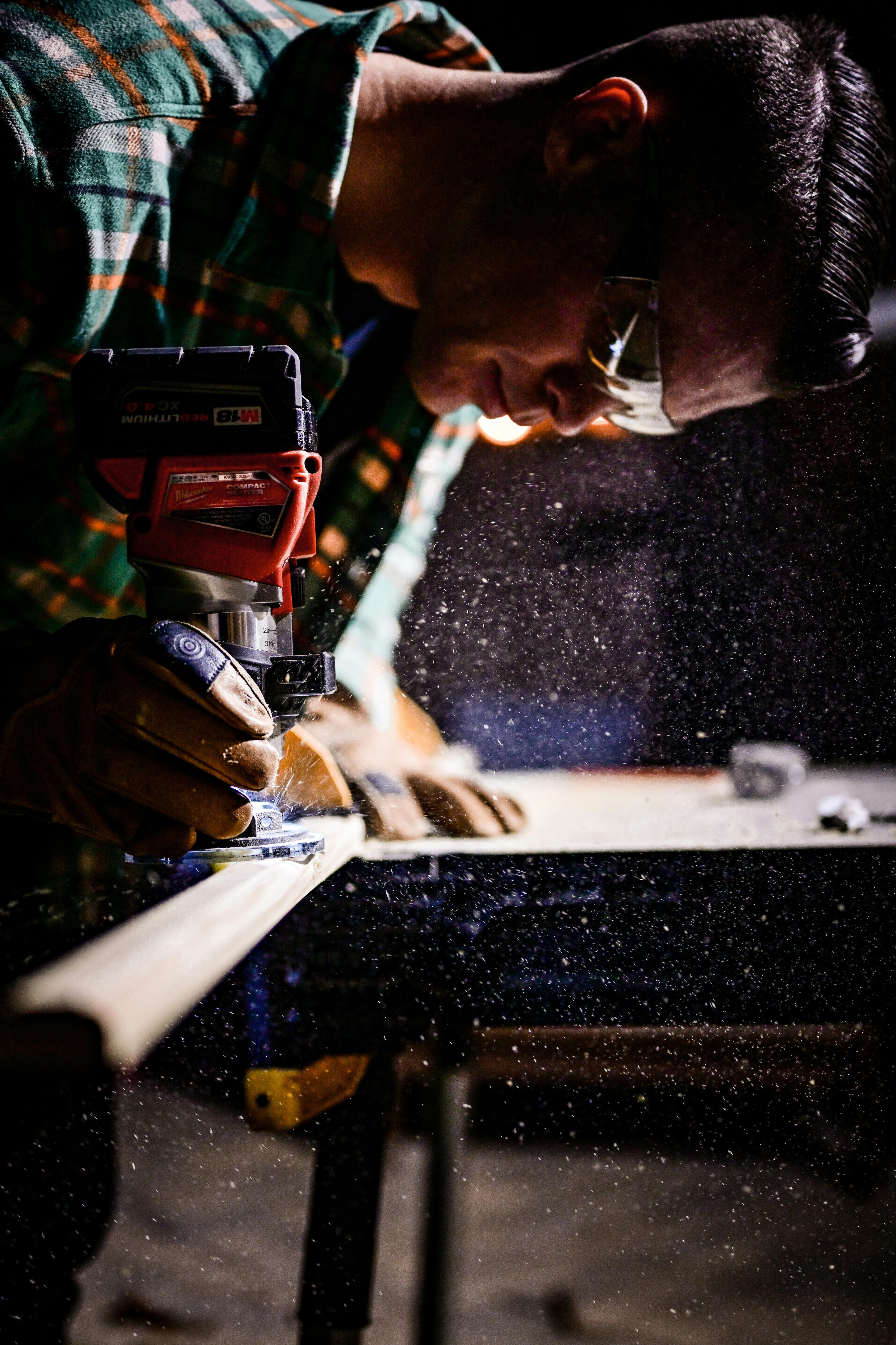 A carpenter uses a handheld power router to shape detailed trim, with sawdust suspended in the air. This image reflects the high-skill, high-value finish carpentry often performed by freelance carpenters on custom projects.
